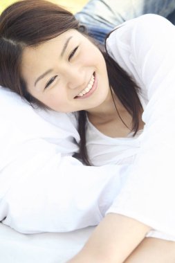 Gülümseyen Asyalı kadın yastıkla yatakta yatıyor.