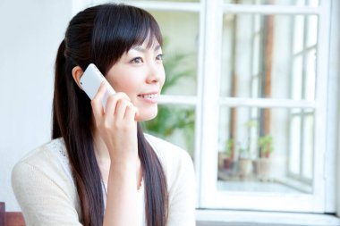 Genç Asyalı kadın evde cep telefonuyla konuşuyor. 