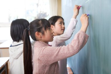 Asyalı kızlar tahtaya tebeşirle resim çiziyorlar. 