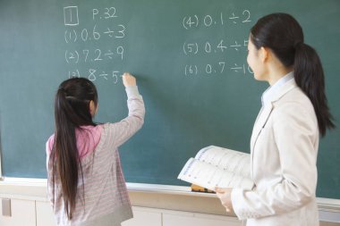 Japon liseli kız ve öğretmen okulda tahtada alıştırma yapıyorlar.