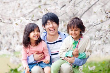 Arka planda çiçek açan kiraz ağacı olan mutlu Asyalı bir aile.