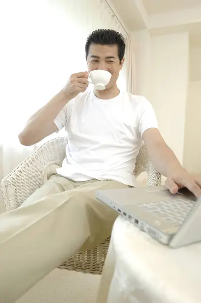 自宅でコーヒーを飲んでいる間 ノートパソコンを使っている男 — ストック写真