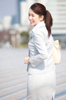 Beyaz takım elbiseli bir kadın şehirde yürüyor.