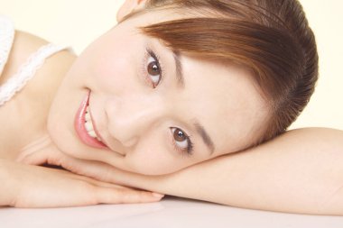 Genç Asyalı bir kadın beyaz arka planda yalnız bir şekilde elleri üzerinde yatıyor. 
