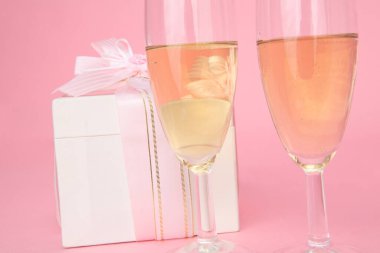 Hediye kutusu ve pembe arka planda şarap kadehleri    