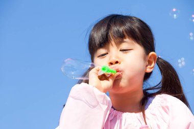 Küçük Asyalı kız dışarıda sabun köpüğü üflüyor.  