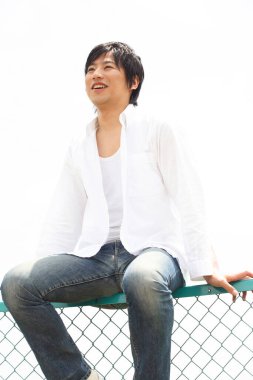 Bir adam dışarıda çitin üzerinde oturuyor.