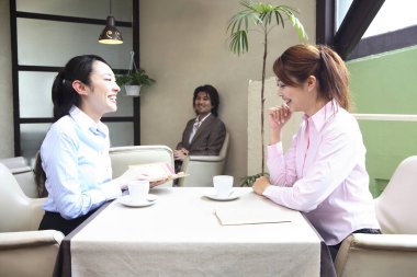 İki kadın kahve fincanlarıyla bir masada oturuyor.