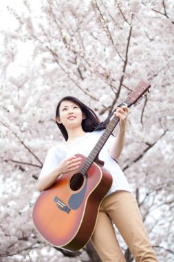 Parkta gitar çalan Asyalı kız. 