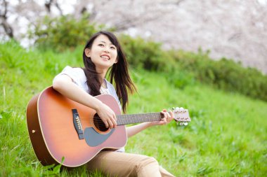 Parkta gitar çalan Asyalı kadın.