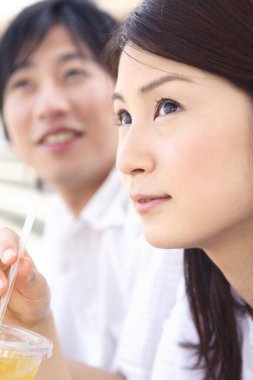 Elinde içki tutan bir kadın ve arkasında oturan bir adam.