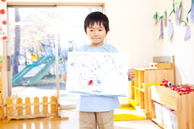 Küçük Asyalı çocuk elinde resmini tutuyor. 