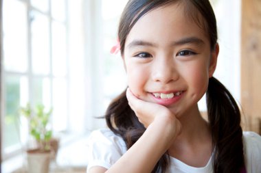 Pencerenin yanında saçları örgülü, gülümseyen kız.
