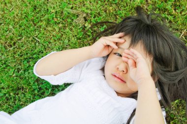 Parkta uzanmış kameraya bakan küçük Asyalı kız. 