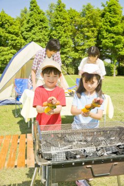 Genç mutlu Japon ailesi kampta barbekü yapıyor.