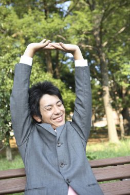 Takım elbiseli bir adam bankta oturmuş dinleniyor.