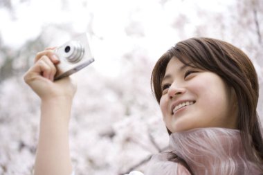 Genç bir kadın parkta pembe çiçeklerle fotoğraf çekiyor.