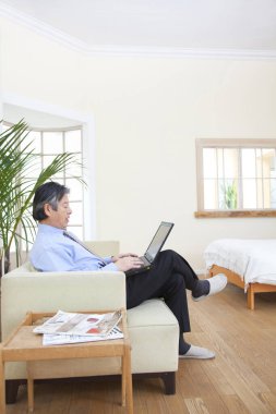 Evde dizüstü bilgisayarla çalışan kıdemli Asyalı adam.