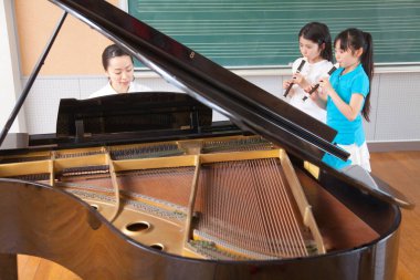 Asyalı kızlar müzik dersi sırasında öğretmenleri onlara piyanoda eşlik ederken flüt çalarlar.. 