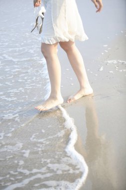 Sahilde yürüyen elbiseli bir kadın.