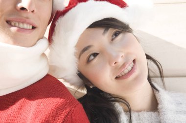 Genç çift Noel kıyafetleri giyip gülümsüyor ve kameraya bakıyor.