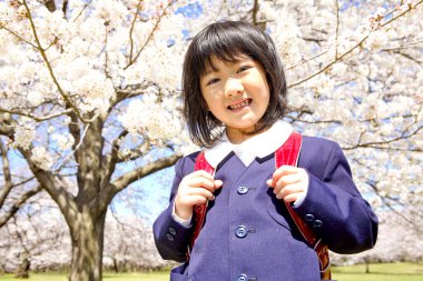 Sırt çantalı tatlı Japon kız çiçek açan bahçede yürüyor.