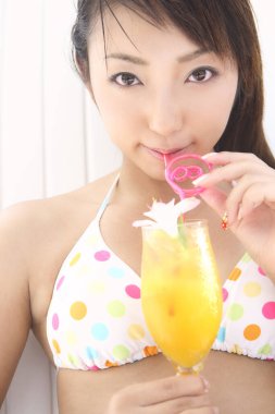 Bikinili Asyalı kadın kokteyl içiyor.