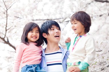 Arka planda çiçek açan kiraz ağacı olan mutlu Asyalı bir aile.