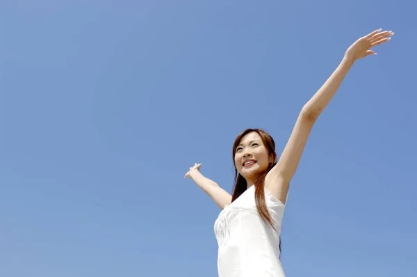 young woman with raised hands against blue sky background.