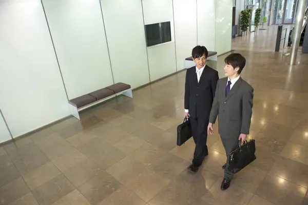 two men in suits walking down a hallway