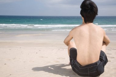 Sahilde oturan Asyalı adamın arkadan görünüşü