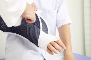 Doktor kol askısı takan hastaya yardım ediyor.