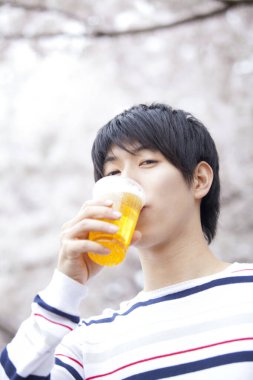 Genç Asyalı adam parkta bira içiyor. 