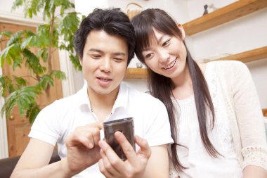 Genç Asyalı çift evde akıllı telefon kullanıyor. 