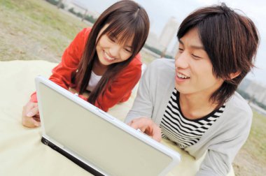 Genç çift dışarıda battaniyeye dizüstü bilgisayar kullanıyor.