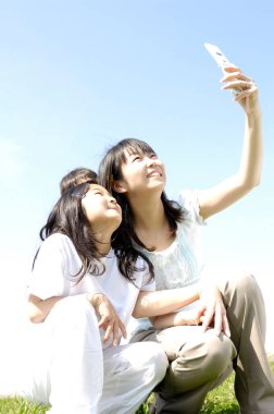 Genç anne ve kızı parkta selfie çekiyorlar.