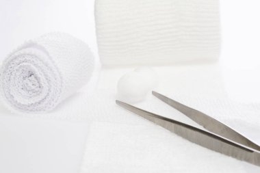 Steril tıbbi bandajlar, pamuk topları ve beyaz bir yüzeyde cımbız..