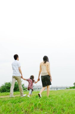 Üç kişilik mutlu bir aile parkta yürüyor.