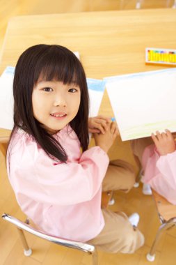 Sınıfta oturmuş resim çizen gülümseyen kız.