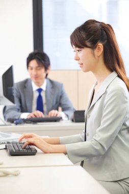 İş kadını masada bilgisayar kullanarak oturuyor.