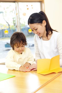 Kadın, çocuğa kağıt işi için yardım ediyor.