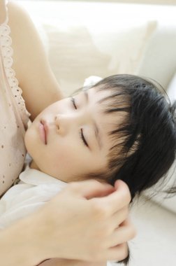 Kızı kollarında uyuyan Asyalı genç bir kadın. 