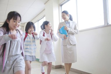 Öğretmen üç tane gülümseyen kızla yürüyor.