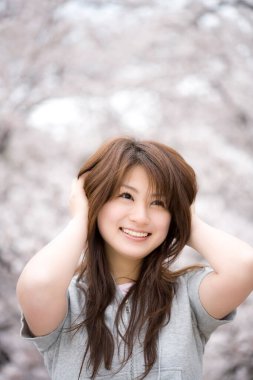 Bulanık kiraz ağaçlarının arka planında güzel genç bir Japon kadın.