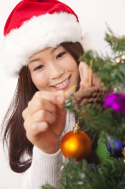 Noel Baba şapkalı Asyalı kız Noel ağacı süslüyor.
