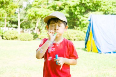 Parkta sabun köpüğü üfleyen yakışıklı Asyalı çocuk.