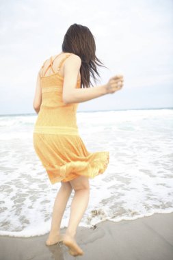Plajda yürüyen elbiseli genç kız.