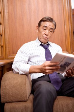 Olgun iş adamı odada kitap okuyor.
