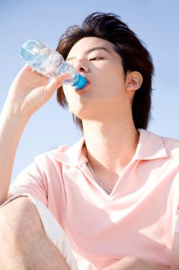 Genç Asyalı adam açık havada su içiyor.