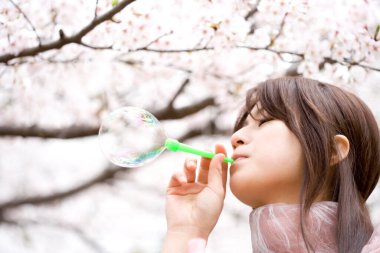 Asyalı kadın dışarıda sabun köpüğü üflüyor.